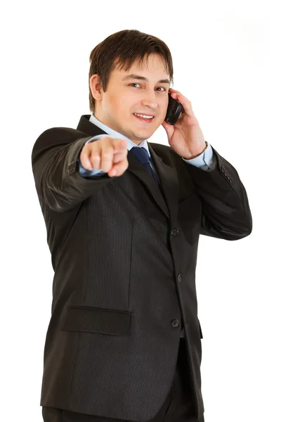 Smiling young businessman talking on mobile phone and pointing finger at yo — Stock Photo, Image