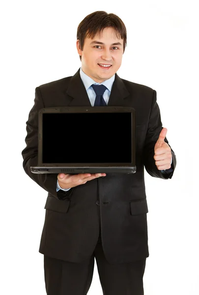 Sonriente joven empresario sosteniendo portátil con pantalla en blanco y mostrando thu — Foto de Stock