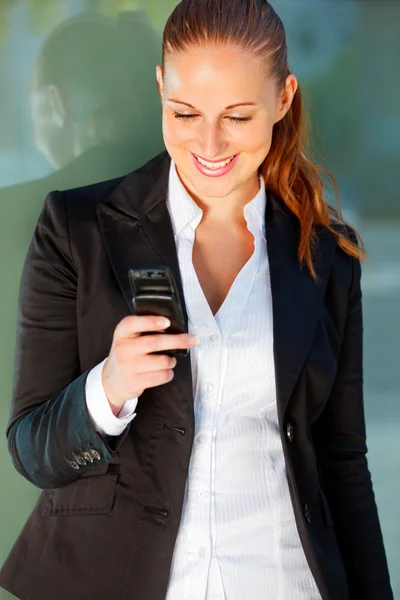 Sorridente donna d'affari vicino edificio per uffici guardando sul cellulare — Foto Stock