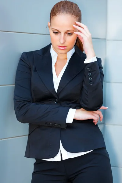 Fundersam affärskvinna med hand nära huvudet stående på office building — Stockfoto