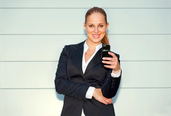 Smiling business woman holding mobile in hand near office building — Stock Photo, Image