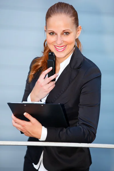 Inclinando-se sobre trilhos no prédio de escritórios sorridente mulher de negócios segurando mobil — Fotografia de Stock