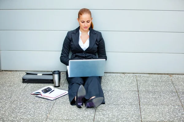Pensive business woman sitting on floor at office building and using lapto — Stock Photo, Image