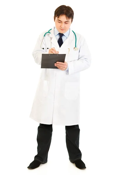 Médecin sérieux avec stéthoscope prenant des notes dans le dossier médical Image En Vente