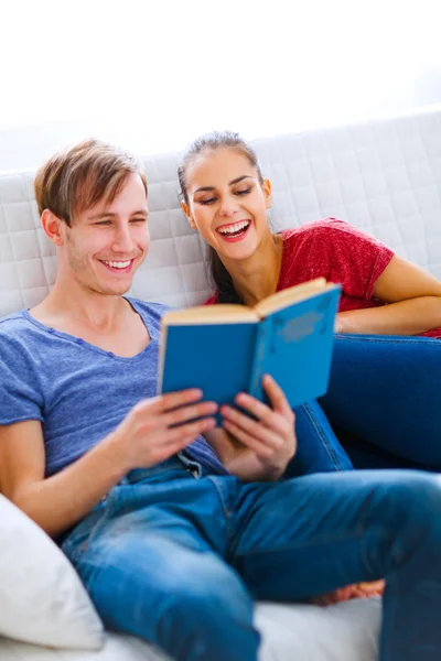 微笑着坐在沙发上的书的年轻夫妇 — 图库照片
