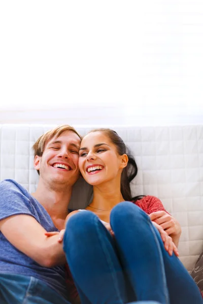 Young couple sitting at couch and laughing — Stock Photo, Image