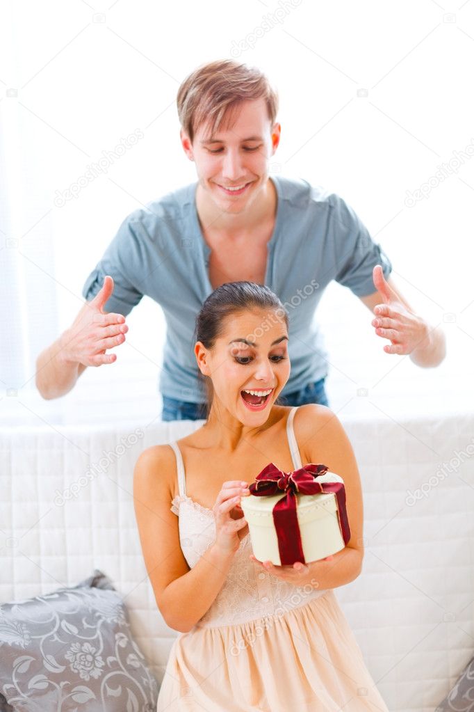 Young man uncover eyes of surprised girlfriend with present in h