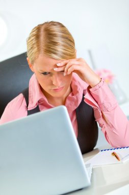 Concerned business woman working on laptop at office clipart