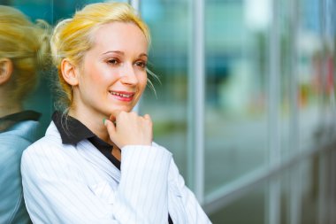 Pensive business woman with hand near face standing near office building clipart