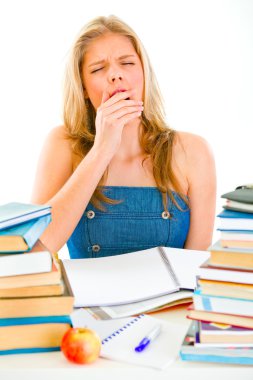 Yawning tired teengirl sitting at table with piles of books clipart