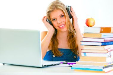 Sitting at table smiling teengirl with headphone listening audio lessons clipart