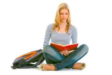 Pensive teengirl with schoolbag sitting on floor and reading book clipart