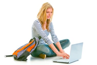 Pensive teenager sitting on floor with backpack and using laptop clipart