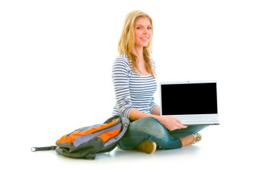 Smiling teen girl sitting on floor and showing laptops blank scr clipart