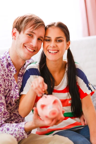 Retrato de feliz pareja joven poniendo moneda en alcancía — Foto de Stock
