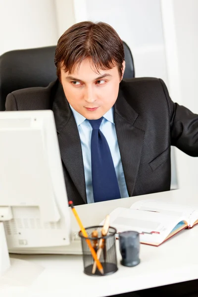 Alert modern businessman sitting at office desk and looking in corner — Stock Photo, Image
