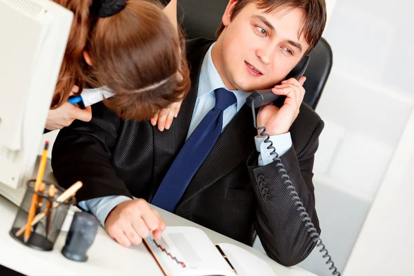 Secretary cleaning chiefs suit while he talking on phone — Stock Photo, Image