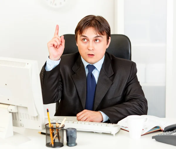 Homem de negócios concentrado com o dedo levantado sentado na secretária do escritório. Idéias — Fotografia de Stock