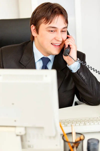 Homem de negócios moderno bem sucedido sentado na mesa de escritório e falando ao telefone — Fotografia de Stock