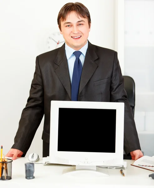Lächelnder Geschäftsmann steht am Schreibtisch und zeigt Monitoren blanke Angst — Stockfoto