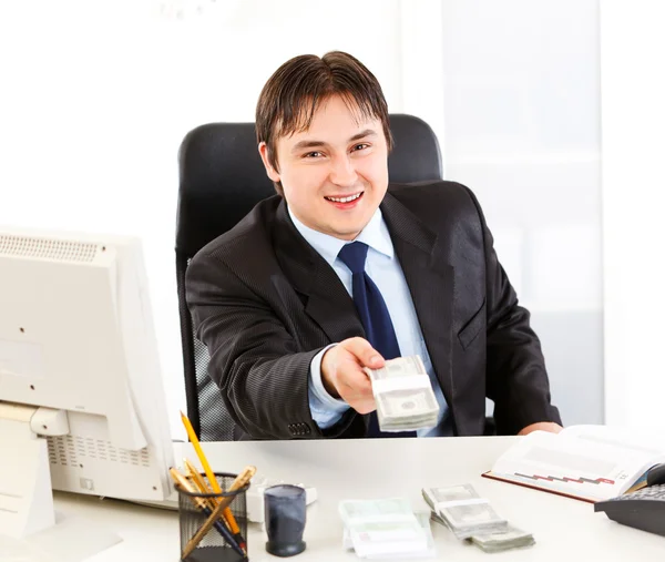 Lächelnder Geschäftsmann sitzt am Schreibtisch und gibt Dollarpäckchen — Stockfoto