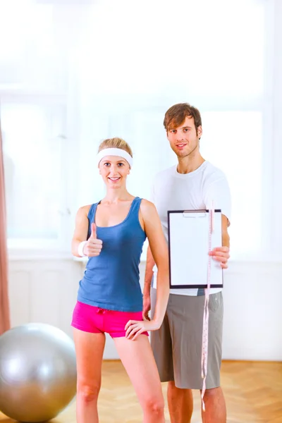 Healthy couple in sportswear showing clipboard with measuring ta — Stock Photo, Image