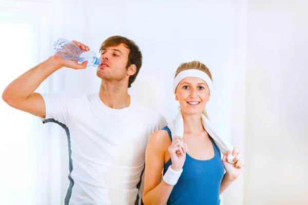 Male athlete drinking water from bottle and smiling girl in spor — Stock Photo, Image