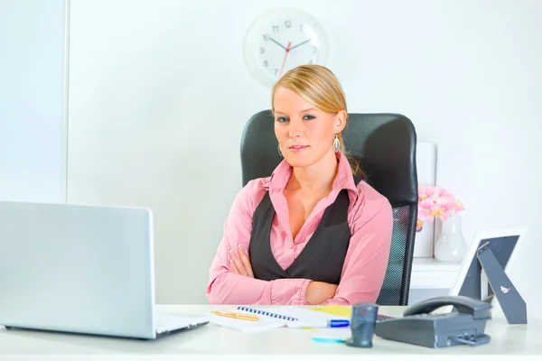 Mujer de negocios bonita sentada en el escritorio de la oficina con brazos cruzados — Foto de Stock