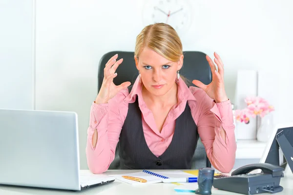 Femme d'affaires en colère assise au bureau et tenant la main près de la tête — Photo