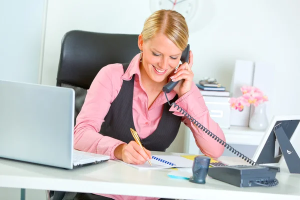 Femme d'affaires souriante parlant téléphone et écrivant au bloc-notes — Photo