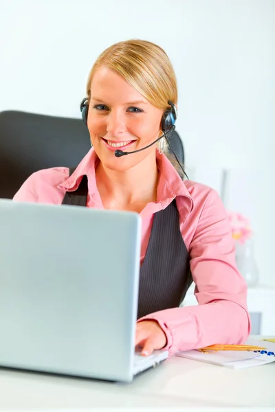 Χαμογελαστή γυναίκα των επιχειρήσεων με το ακουστικό που εργάζονται στο lap-top — Φωτογραφία Αρχείου