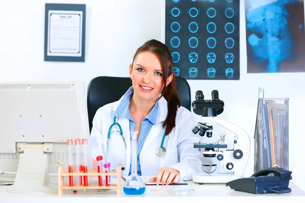 Lächelnde Ärztin sitzt am Tisch in ihrem Büro — Stockfoto