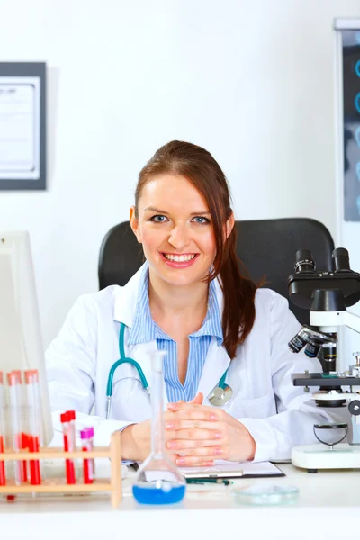 Uśmiechnięta kobieta lekarz siedzi przy stole w jej szafce — Zdjęcie stockowe