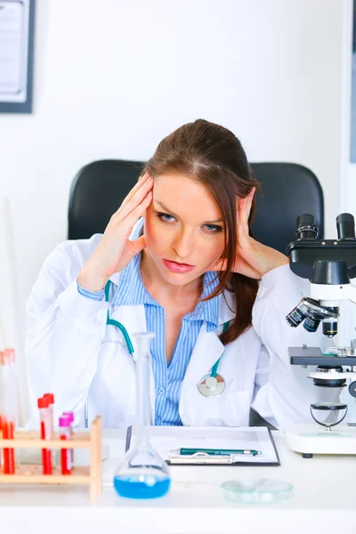Chockad doktor kvinna sitter vid office bord och hålla händerna nära huvud — Stockfoto