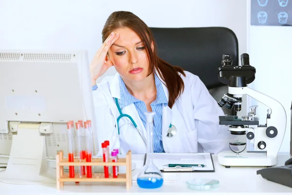 Besorgte Ärztin sitzt am Bürotisch und hält Hand an — Stockfoto