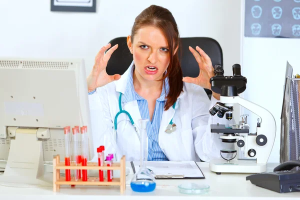 Stressed female medical doctor sitting at office table and holdi — Stock Photo, Image