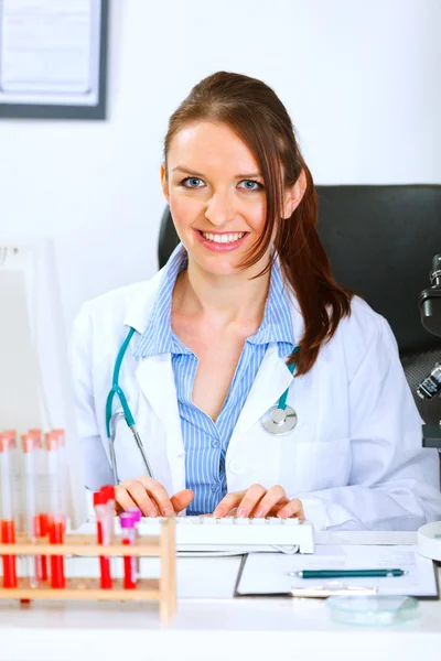 Lächelnde Ärztin sitzt am Bürotisch und arbeitet an einem Comp — Stockfoto