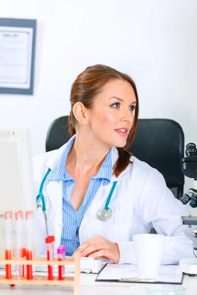 Doctor woman sitting at office table and looking away — Stock Photo, Image