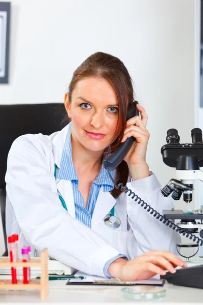 Female medical doctor sitting in cabinet and making phone call — Stock Photo, Image