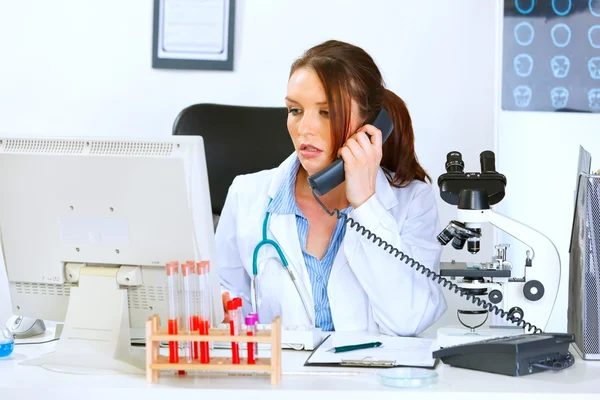 Mujer médica preocupada hablando por teléfono y mirando en el monitor —  Fotos de Stock