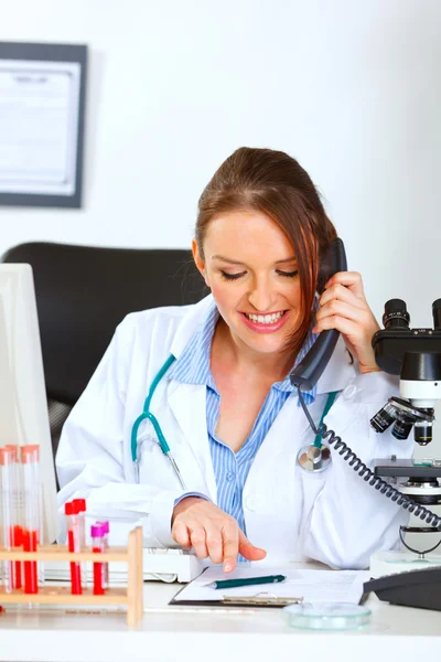 Smiling female medical doctor talking on phone and looking in cl — Stock Photo, Image