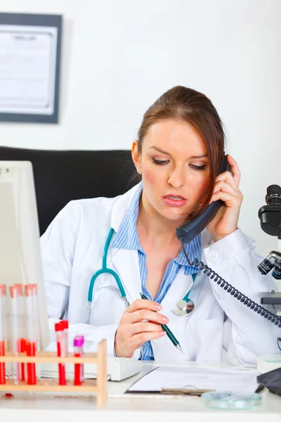 Kobieta lekarz siedzi w biurze i podejmowania rozmowy telefonicznej — Zdjęcie stockowe