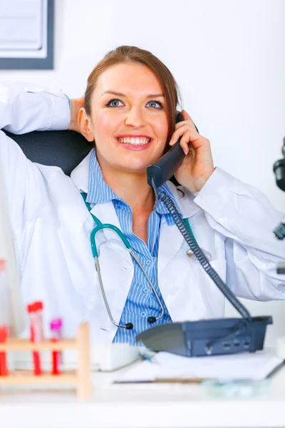 Relaxado médico mulher sentado na mesa do escritório e falando ao telefone — Fotografia de Stock