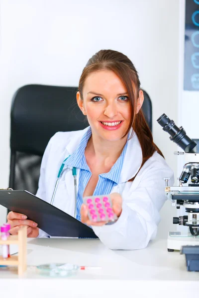 Mujer doctora sonriente sentada en la mesa del consultorio y dando medicamentos recetados — Foto de Stock