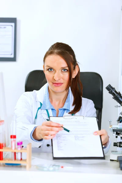 Médico médico mujer sentada en la mesa del consultorio con documento y pluma para firmar — Foto de Stock