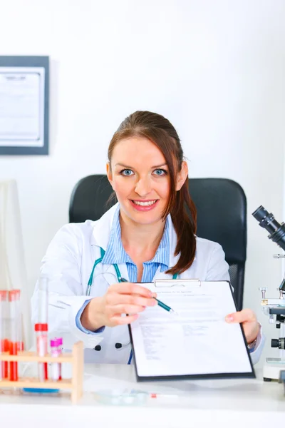 Leende läkare kvinna sitter vid office bord med dokument och penna — Stockfoto