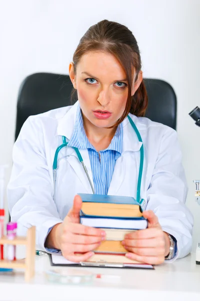 Geschokt arts vrouw zitten aan office tafel met stapel boeken — Stockfoto