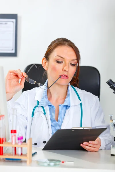 Thoughtful female medical doctor looking in clipboard at cabinet — Stock Photo, Image