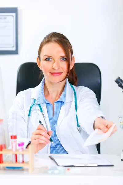 Sorrindo médico mulher sentada à mesa e dando receita médica — Fotografia de Stock