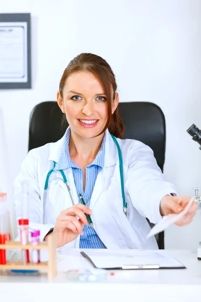 Mujer doctora sonriente sentada en la mesa y dando prescri médica — Foto de Stock